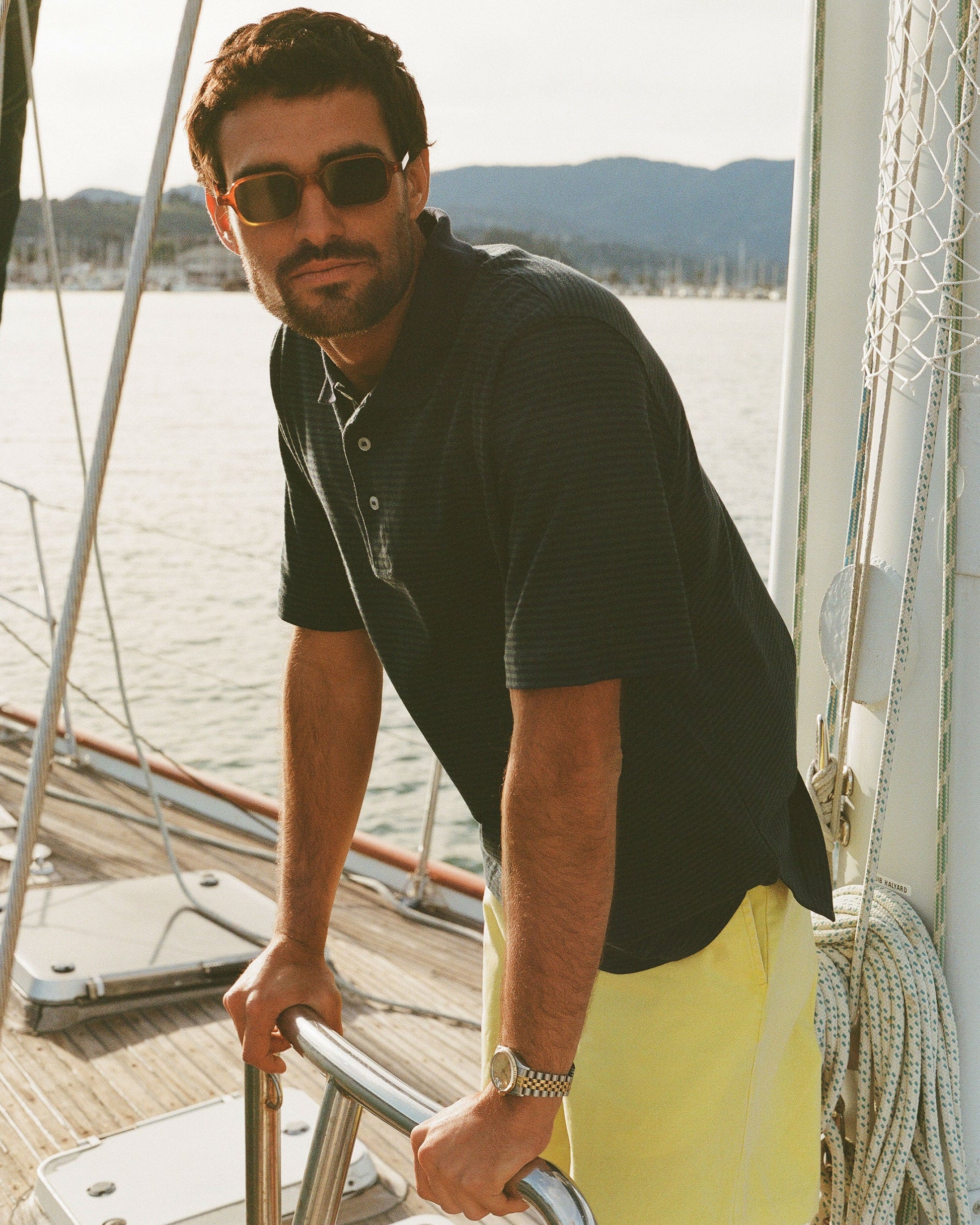 Man on a boat wearing sunglasses and a black shirt with yellow pants